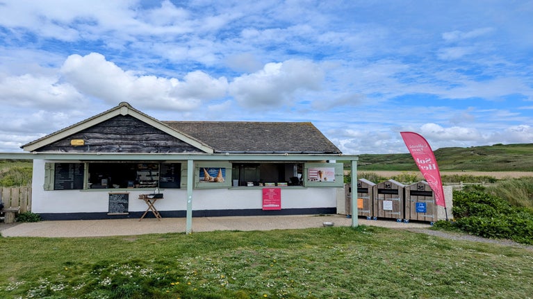 A small building with a veranda and two shuttered windows open, with signs and a table in front.